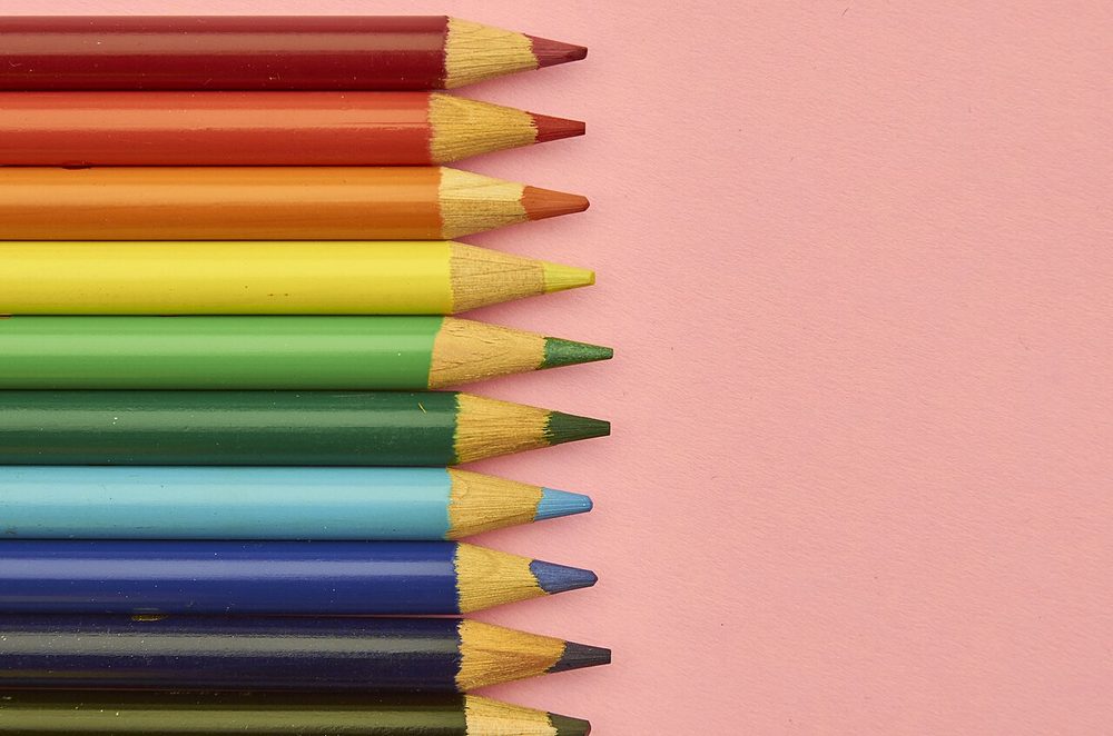 Coloured pencils lined up in a row on a pink surface